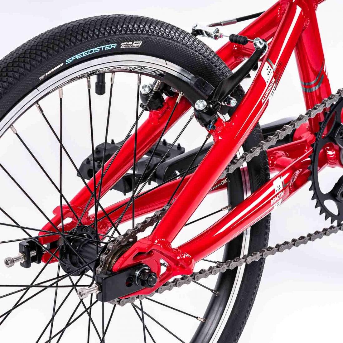 Close-up of a red Inspyre Neo Pro Bike BMX race bike's rear wheel, gear cassette, and chain.
