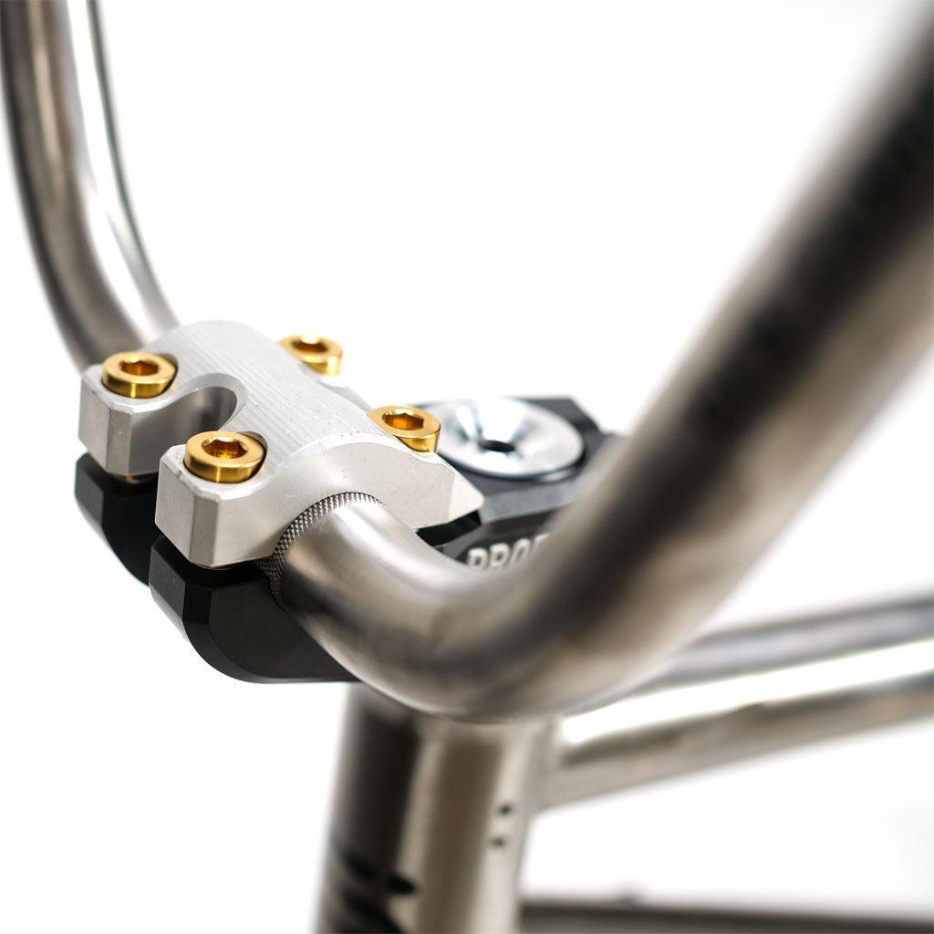 Close-up of the ION BMX TiXX 20 Inch Bike titanium frame handlebars attached to a stem with silver and gold-colored bolts.