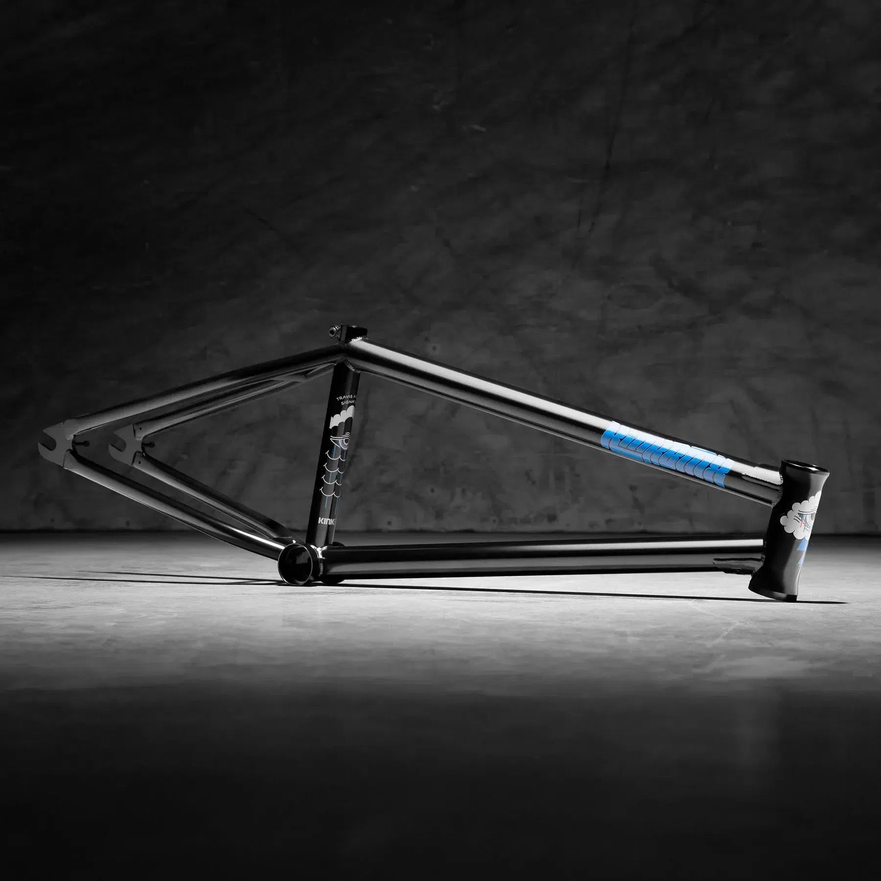The Kink Cloud Frame (Travis Hughes) is a black BMX bike frame made from durable 4130 Chromoly Tubing, featuring a blue accent on the chainstay, resting on a concrete floor against a dark textured background—perfect for street riders seeking reliability.