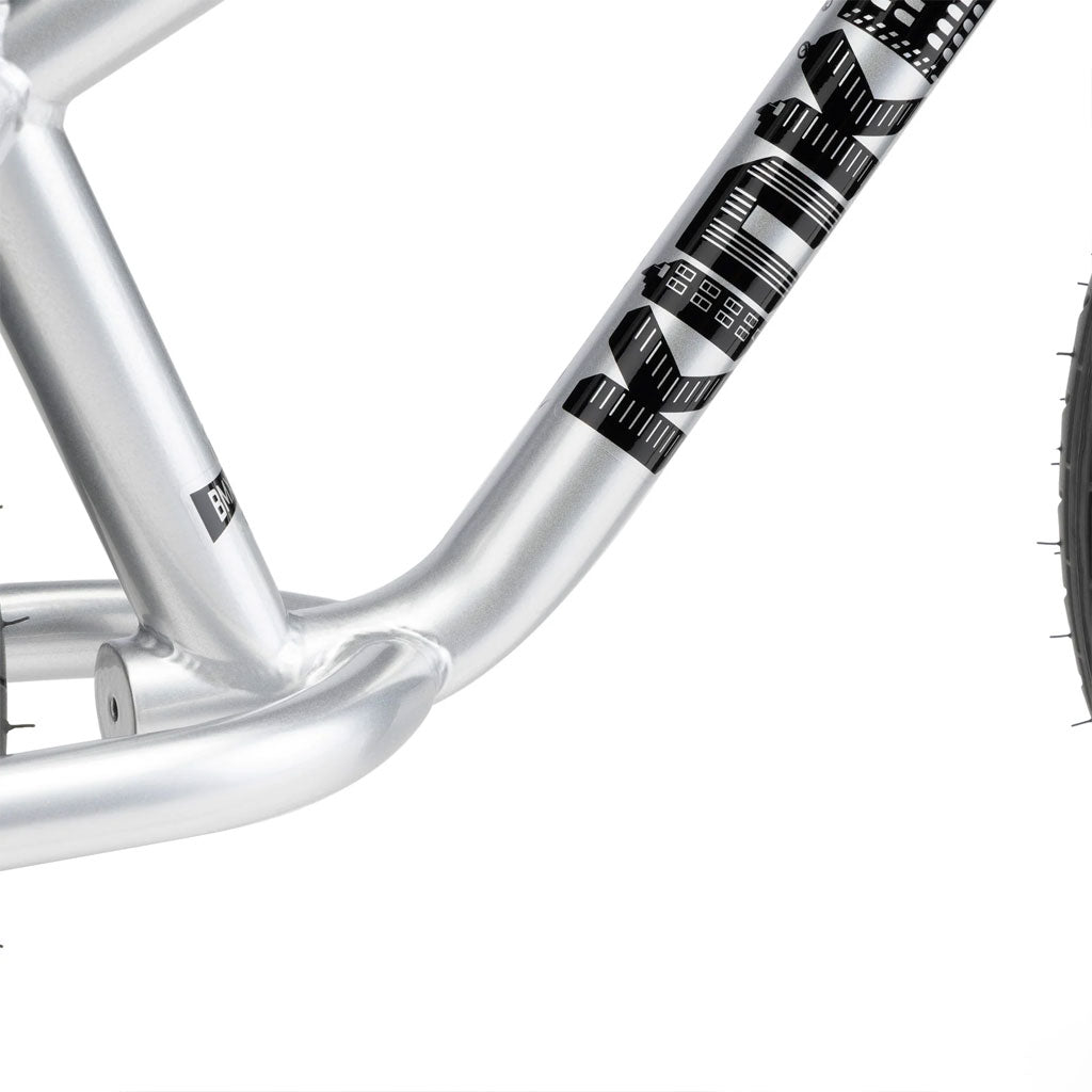 Close-up of the Kink Coast 12 Inch Balance Bike's silver frame with a black geometric pattern and sleek text design. Partial wheel on the right highlights the agility typical of balance bikes.