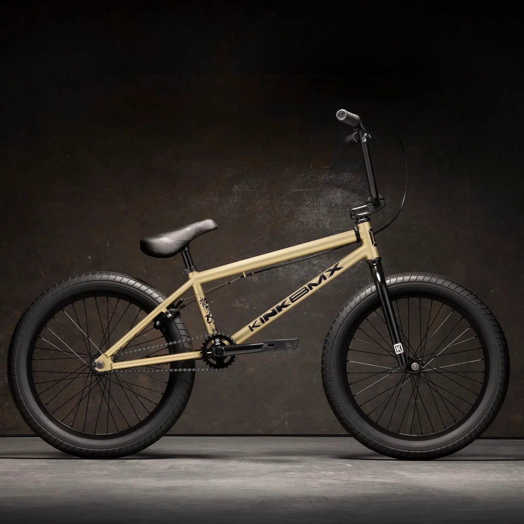 The Kink Curb 20 Inch Bike features a tan BMX design with Kink Ace Grips and Mission Tracker Tyres, highlighted against a dark background.