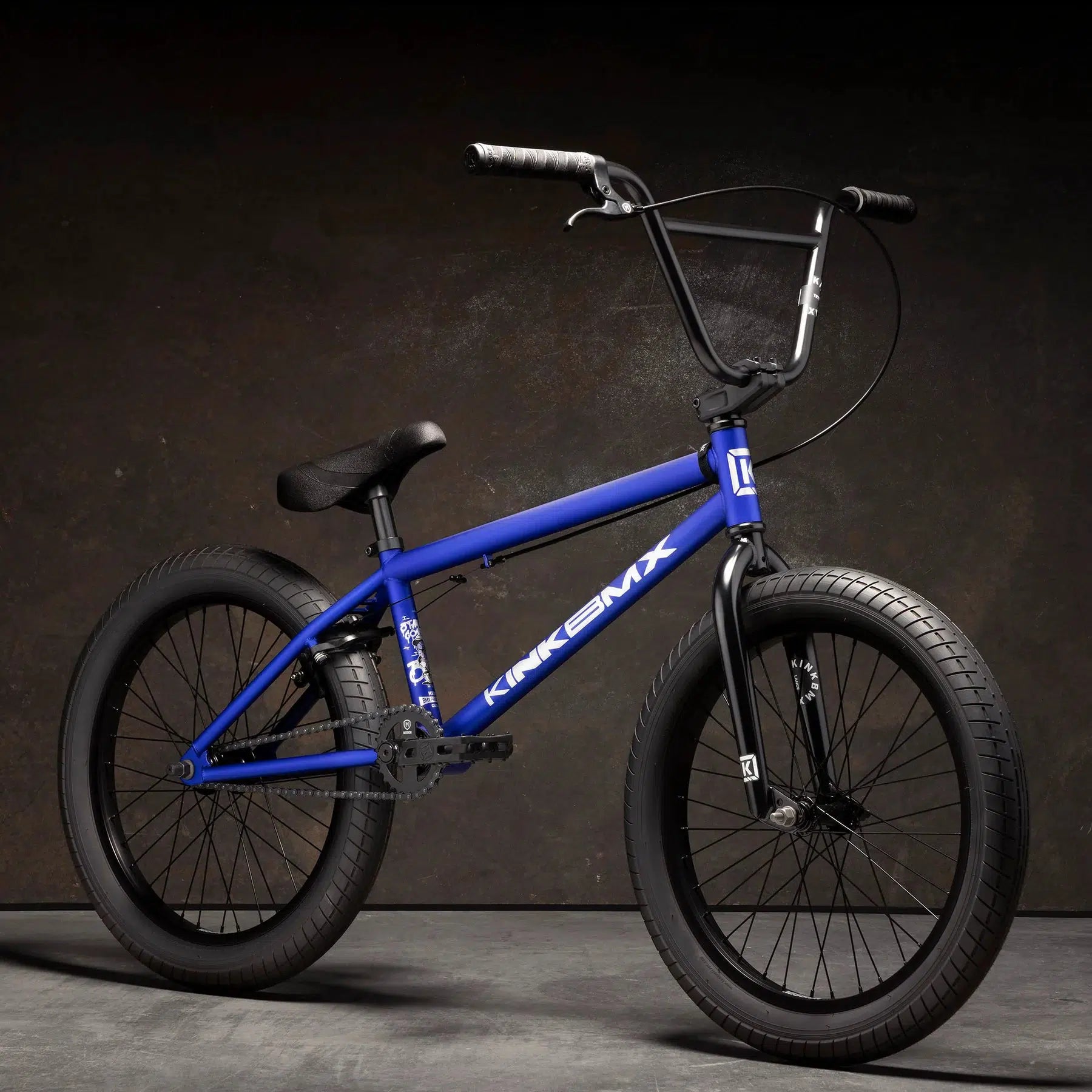 Kink Curb 20 Inch Bike with blue frame, equipped with Kink Ace Grips and black handlebars, featuring Mission Tracker Tyres, set against a dark background.