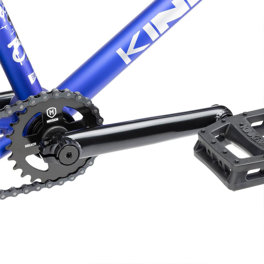 Close-up of the Kink Curb 20 Inch Bike's pedal and crankset, showcasing a black chainring and crank arm attached to its blue frame. The textured black pedal provides excellent grip on this BMX bike.