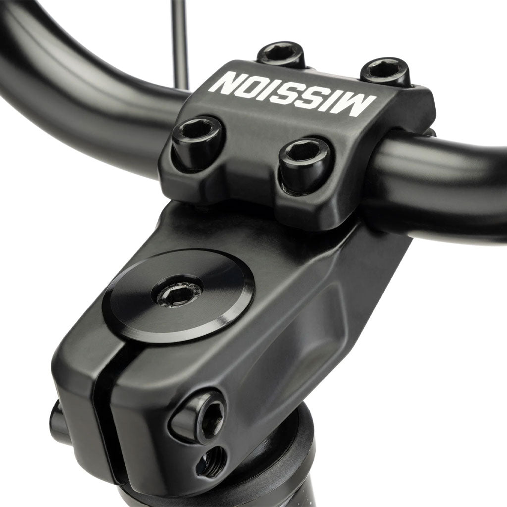 Close-up of the handlebar from a Kink Curb 20 Inch Bike with the brand name "MISSION" printed upside down on the handlebar clamp. The bike's black components feature a matte finish.