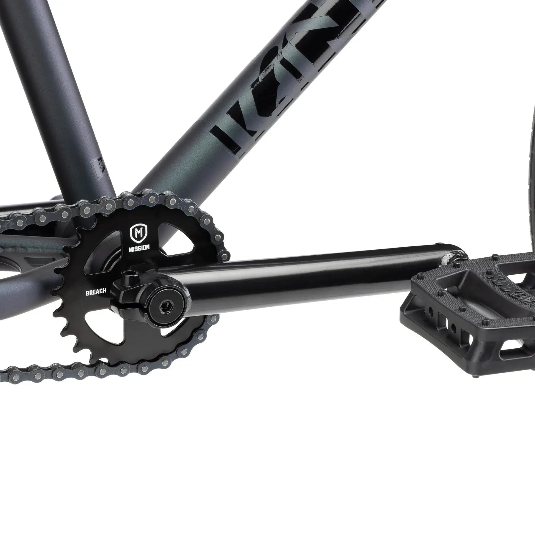 Close-up of a bicycle crankset with a Mission brand chainring and pedal attached to the black frame of the versatile Kink Drifter 26 Inch Bike.