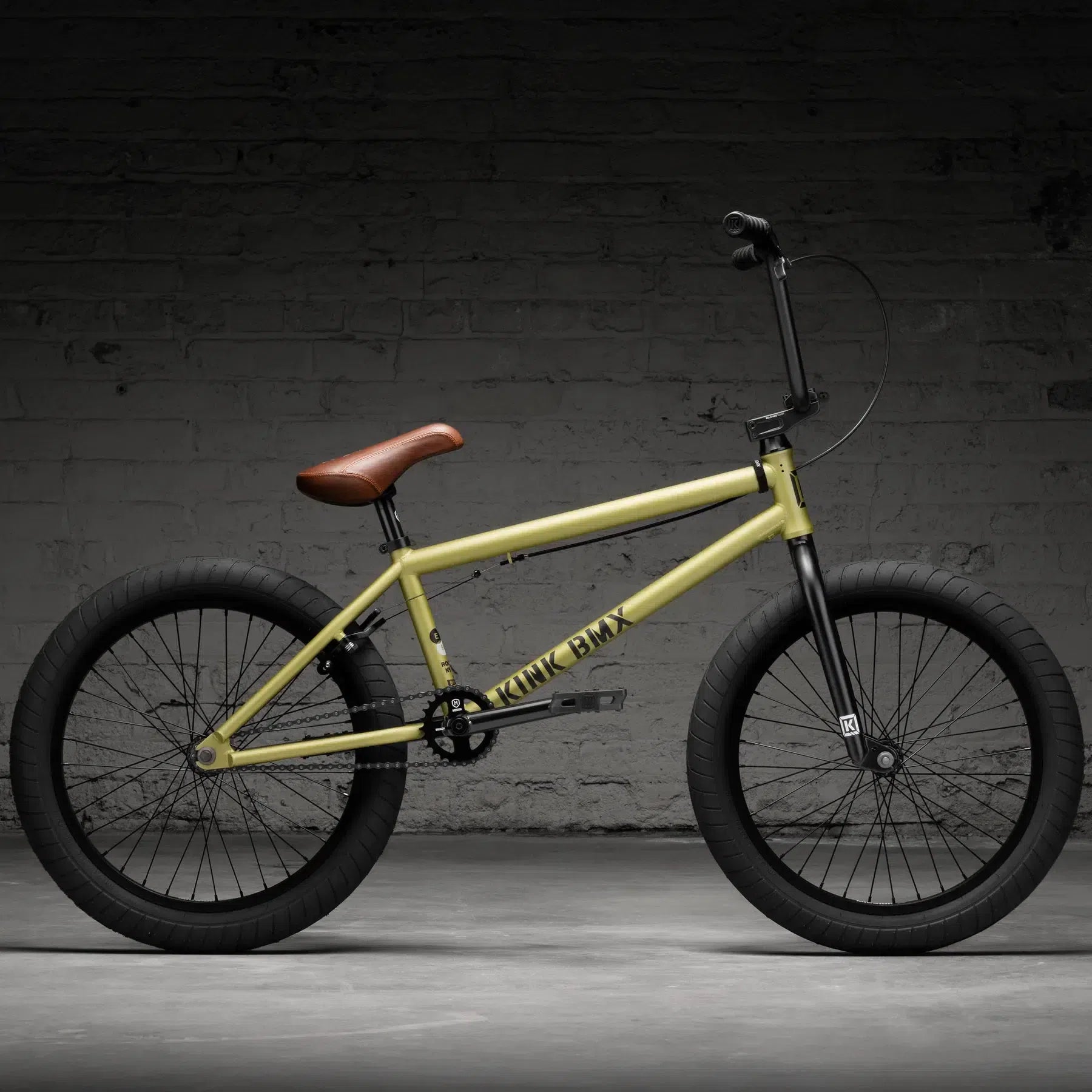 The Kink Gap 20 Inch Bike (2026), in yellow chromoly steel, showcases a brown leather seat and black tires, set against a dark brick wall.