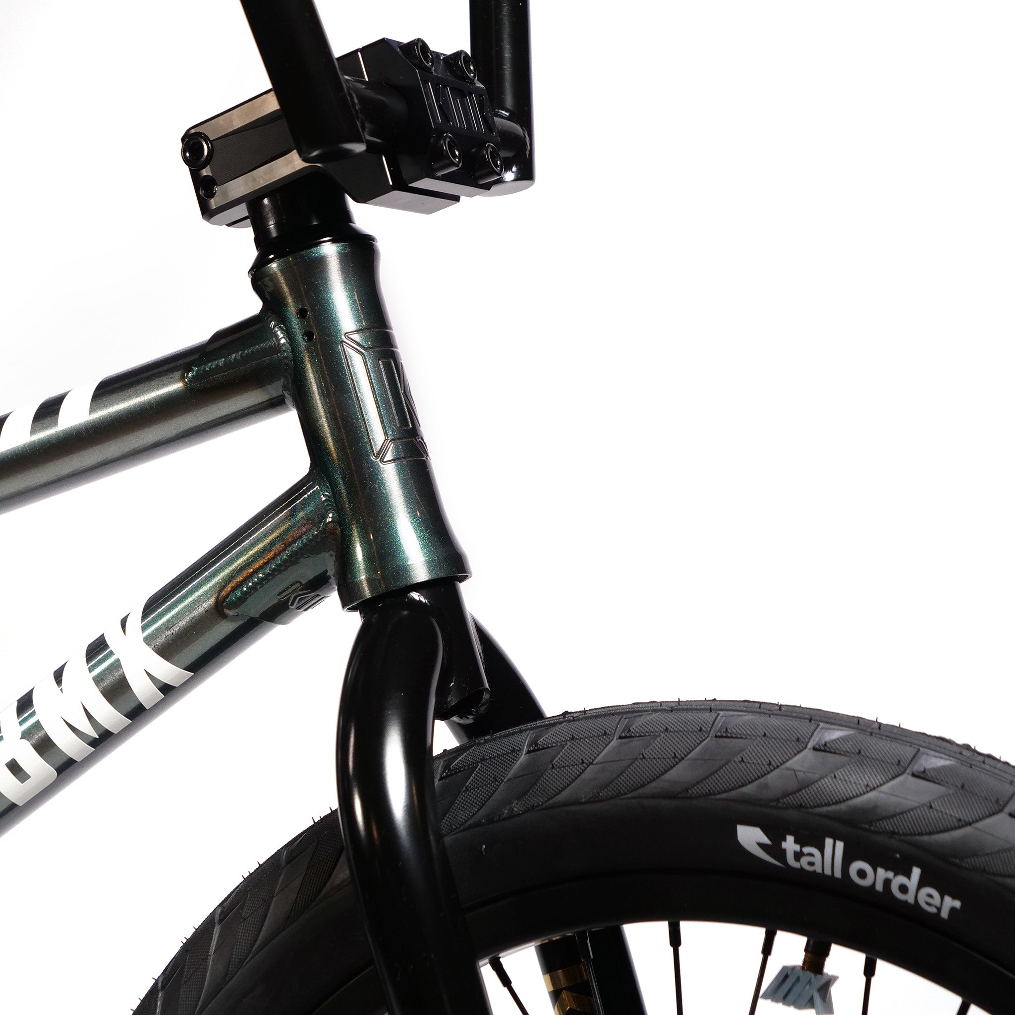 Close-up of a BMX bike showcasing its front frame, fork, handlebars, and part of the front wheel. The tire is branded "tall order". Featuring a Kink Tactic Custom 20 Inch Bike design, the metallic finish on the frame highlights visible brand markings for a budget-friendly custom build.