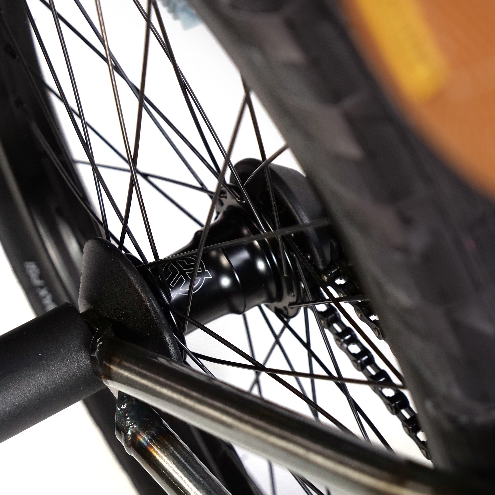 Close-up of a bicycle wheel hub, spokes, and part of the tire, highlighting the axle and black metal components on this Kink Tactic Custom 20 Inch Bike.