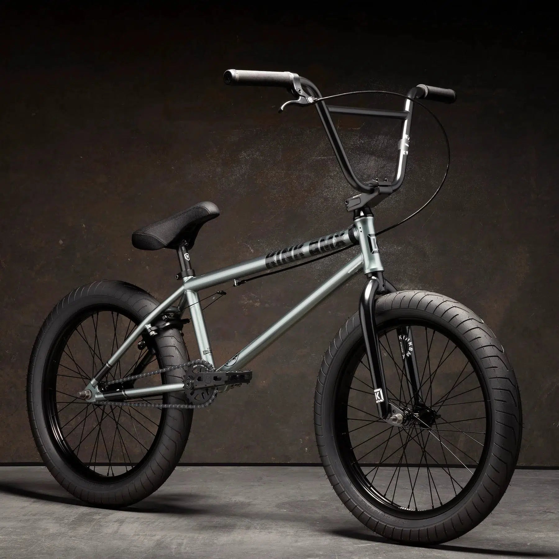 The Kink Whip 20 Inch Bike, featuring a sleek chromoly frame, black handlebars, and thick black tires, is stealthily showcased against a dark background.