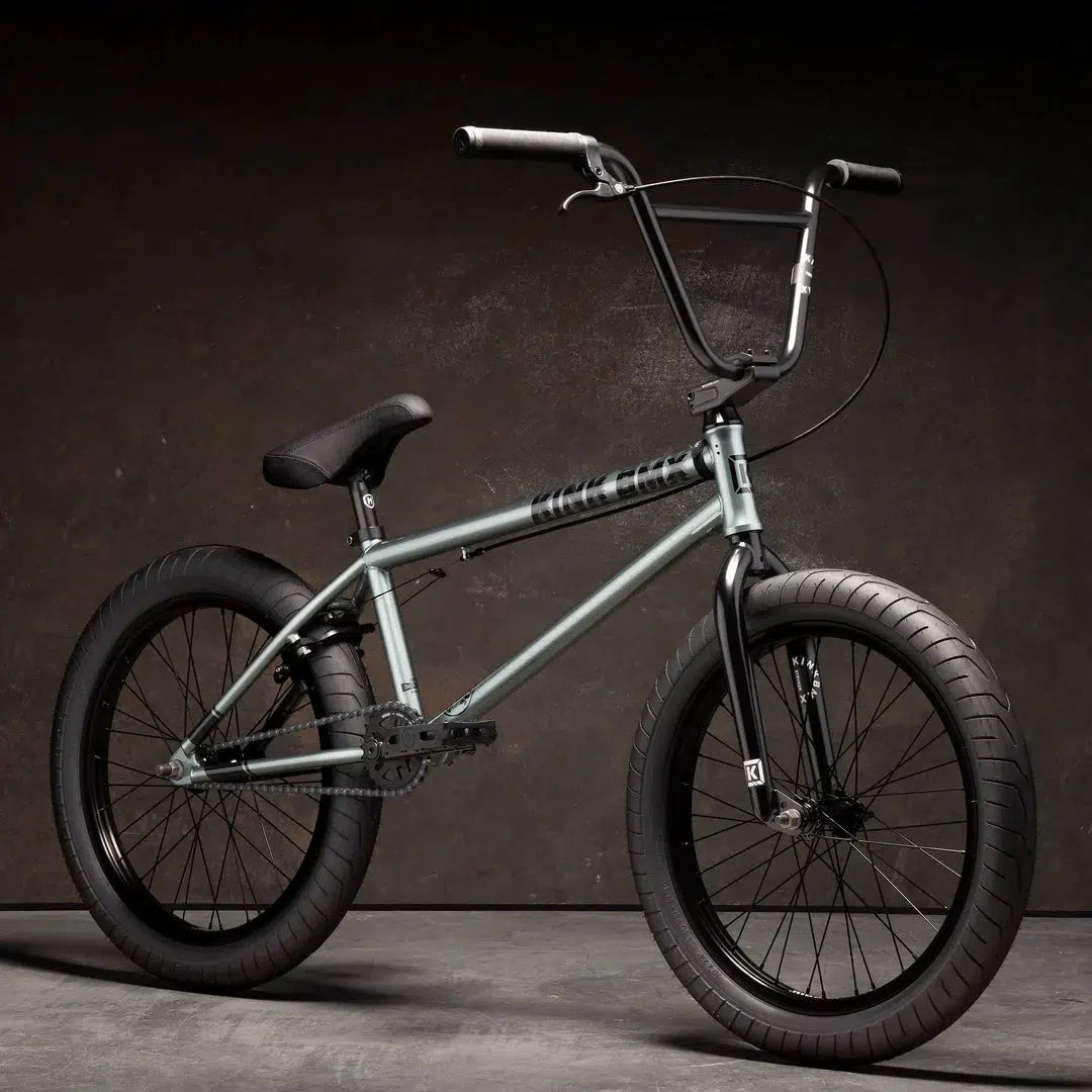 The Kink Whip XL 20 Inch Bike, showcasing a durable Chromoly frame and Mission Mylar rims, stands out against a dark background with its black handlebars and thick tires.