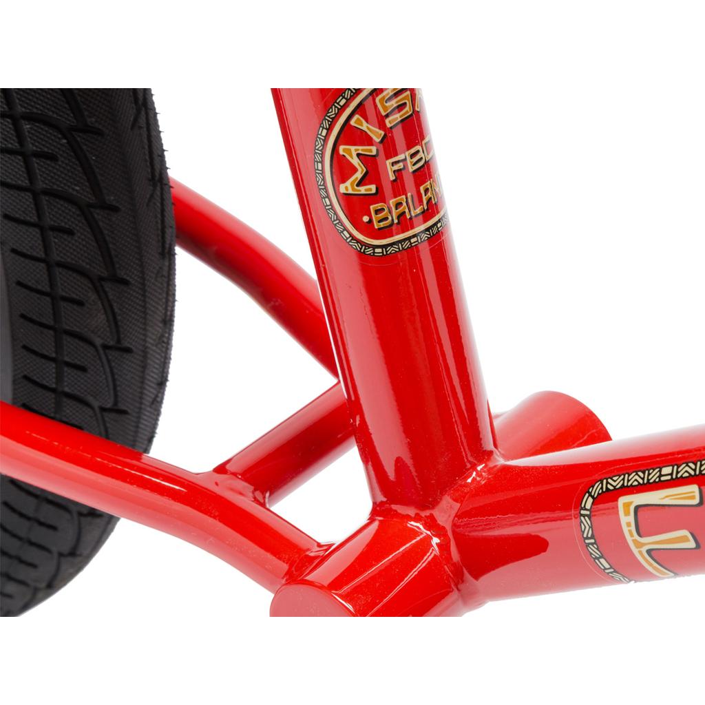 Close-up of the Fit Misfit 12 Inch Balance Bike's red frame with a black tire, showcasing brand decals and smooth TIG welded steel tubing details.