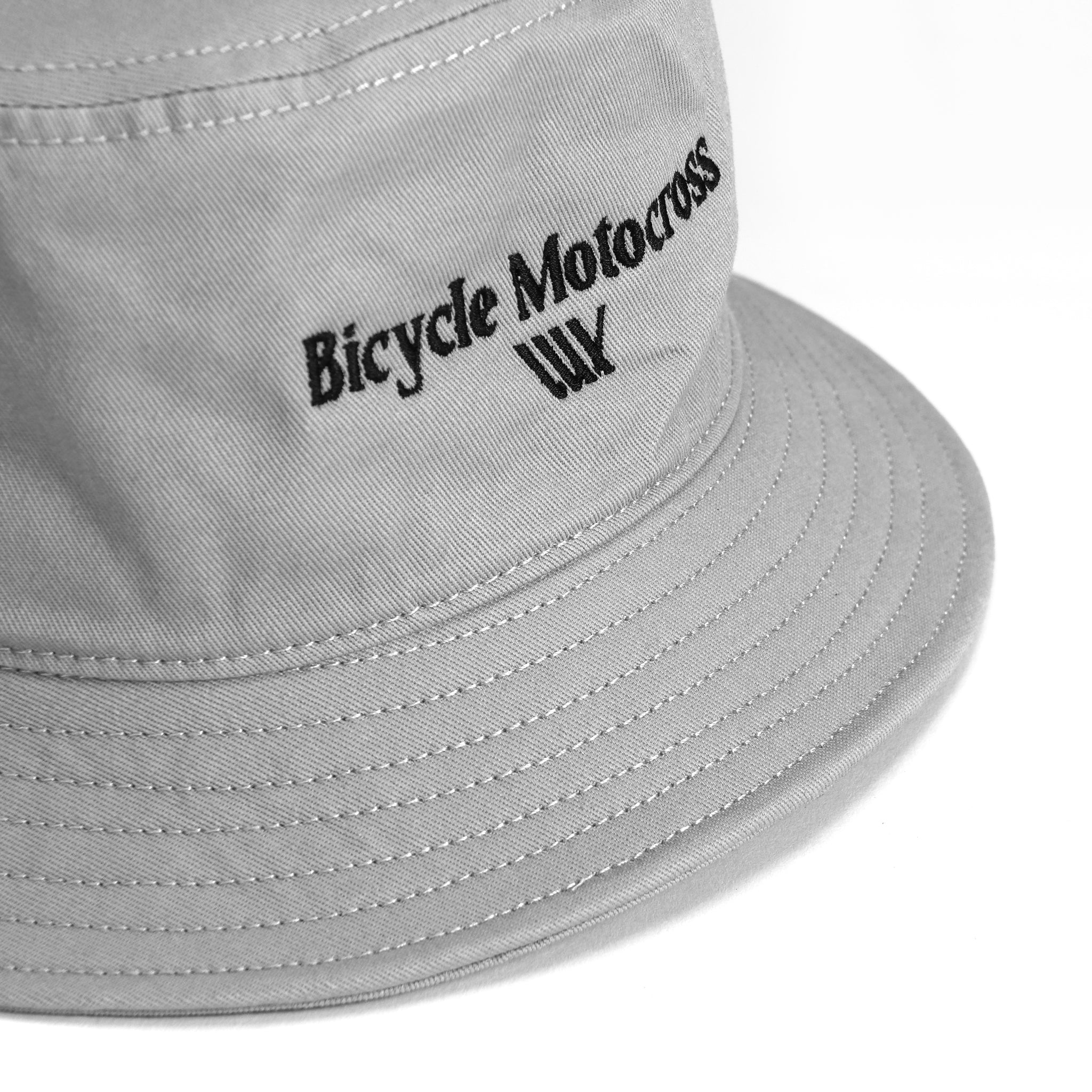 Introducing the LUXBMX Bicycle Motocross Bucket Hat Storm, a stylish grey hat featuring "BMX" stitched in black font on the front with a distinctive three-wave design below the text.