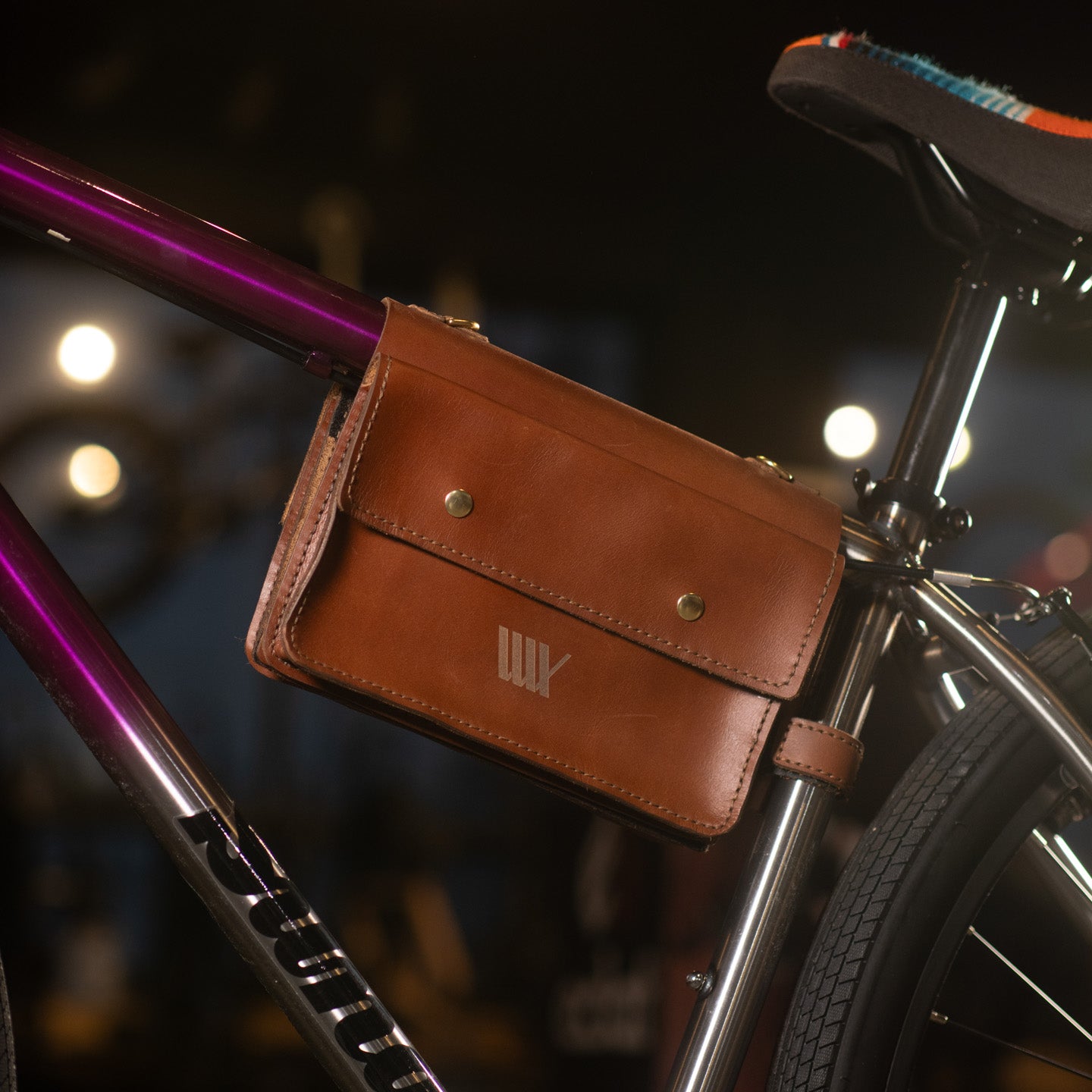 A handcrafted LUXBMX Deluxe Leather Frame Bag in brown is attached below the bicycle seat, showcasing Queensland craftsmanship against a softly blurred background.