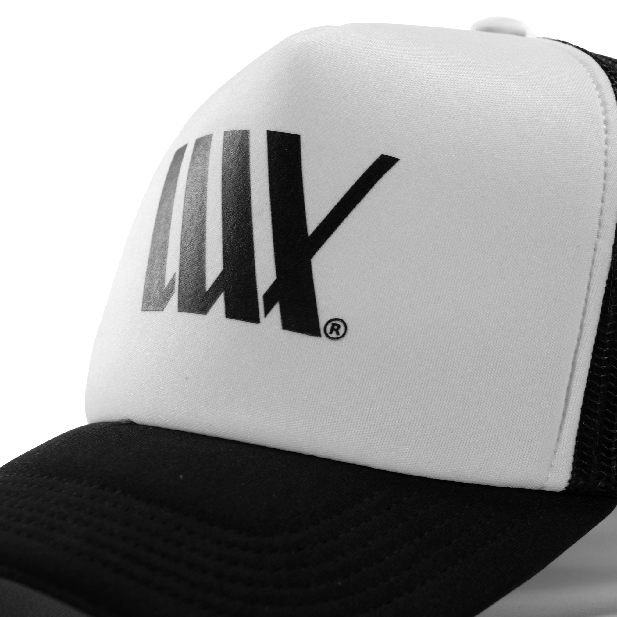 Close-up of the LUXBMX Flag Trucker Cap Black, highlighting its black and white design with a classic fit. The cap features a white front panel adorned with a black stylized "LUX" logo, while the back is crafted from recycled polyester mesh fabric.