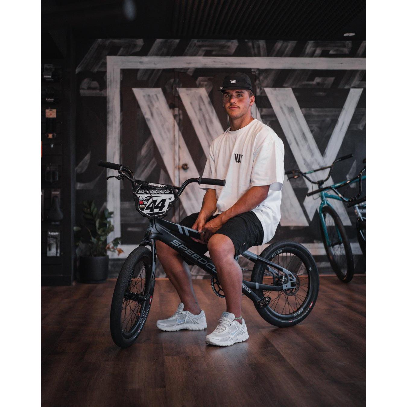 A man, part of the LUXBMX Izaac X Rico Kids Tee team, sits on a bike in a store.