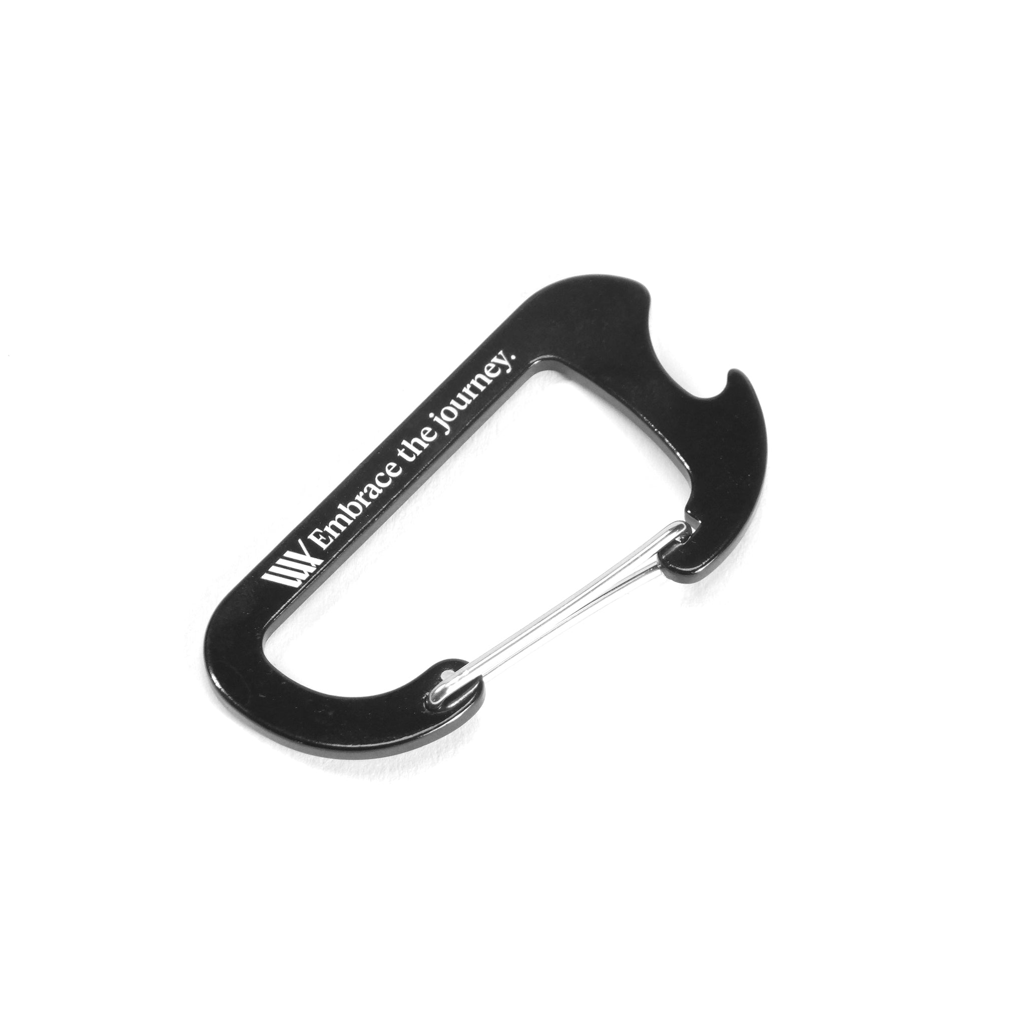 The LUXBMX Journey Bottle Opener Carabiner is a black metal carabiner with a silver spring clip and "Embrace the journey." printed on the side—ideal for any adventure.