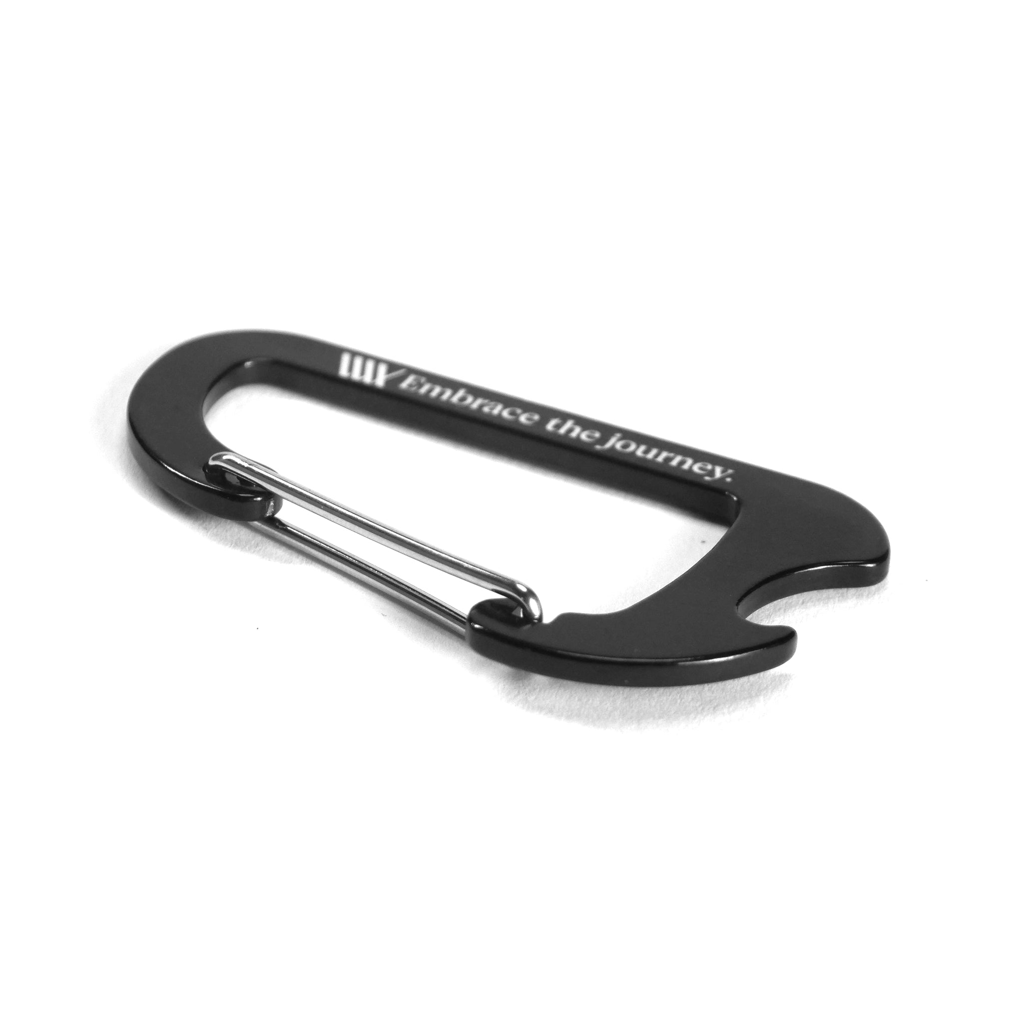 A black LUXBMX Journey Bottle Opener Carabiner with "Embrace the journey." engraved on its side, shown on a white background.