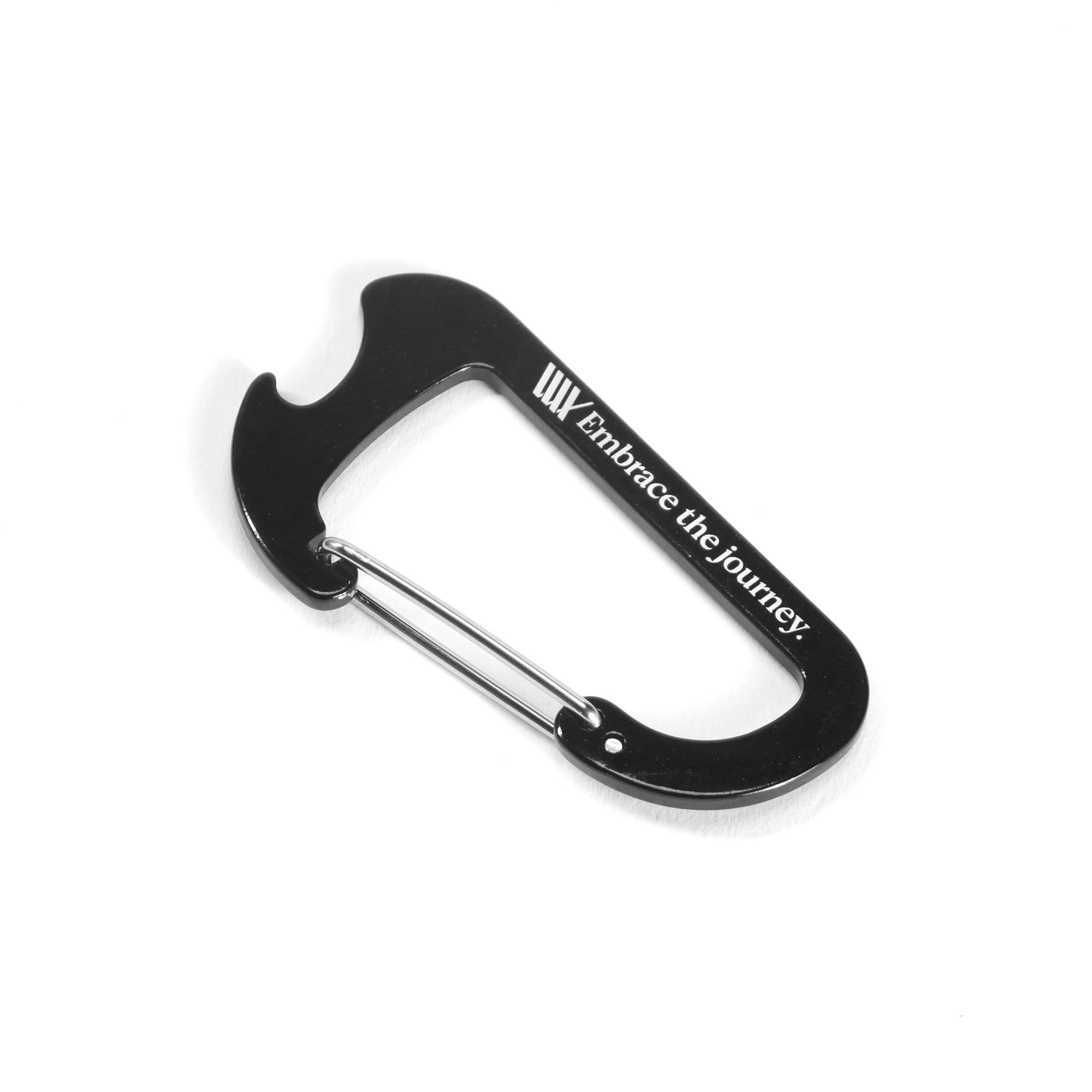 The LUXBMX Journey Bottle Opener Carabiner, shown in black with a metal clasp and “Embrace the journey.” plus LUXBMX branding on its side, is displayed against a white background.