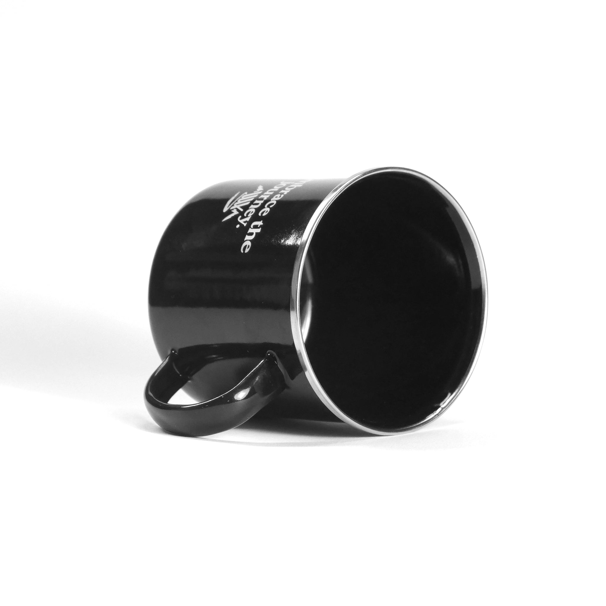 The LUXBMX Journey Camp Mug, a black ceramic mug with the handle to the left, is shown lying on its side against a plain white background, evoking classic campfire style.