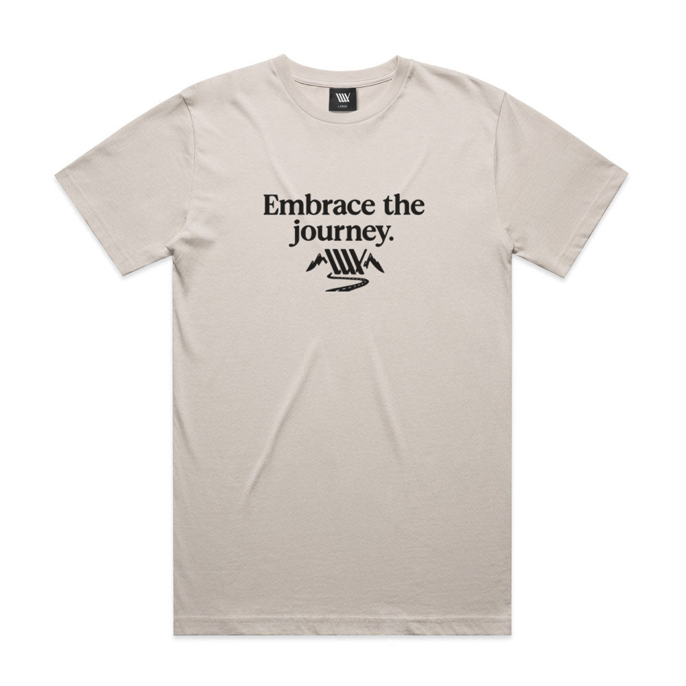 The LUXBMX Journey Tee - Bone is crafted from 100% combed cotton and features black "Embrace the journey." text above a minimalist mountain and winding road graphic. Enjoy comfort and style with this premium relaxed fit tee.
