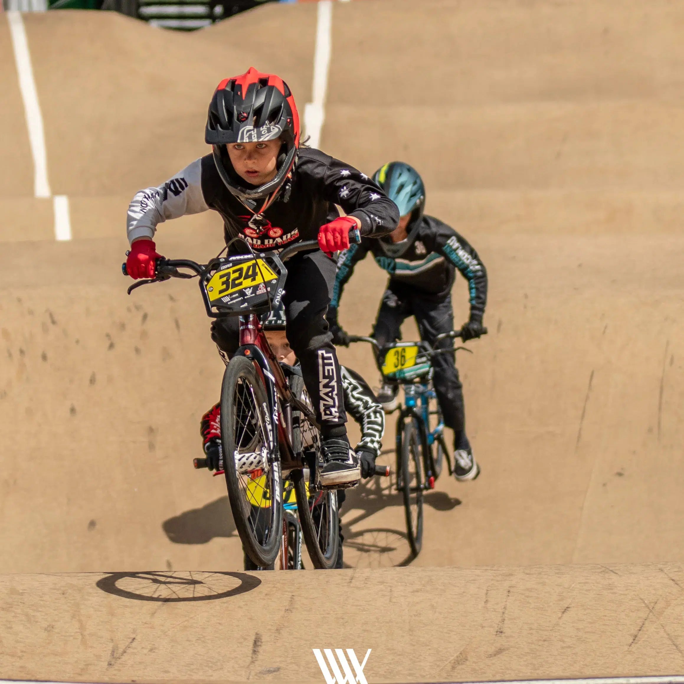 Capture dynamic race action at the Lake Macquarie National Series May 2025 with LUXBMX Race Photo Packages, featuring young cyclists in helmets and uniforms riding BMX bikes—one leading, another close behind on the dirt track.