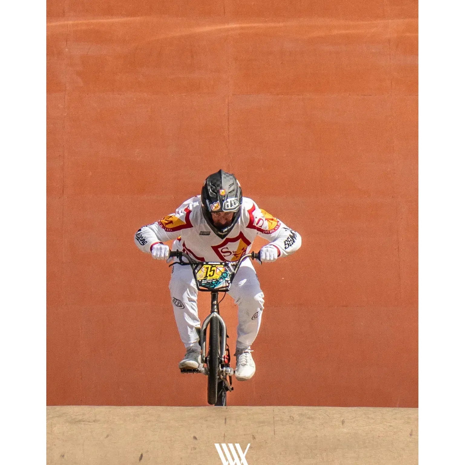 A BMX rider in white and red gear races toward the camera against an orange backdrop, reflecting the excitement of LUXBMX Race Photo Packages – Lake Macquarie National Series May 2025.