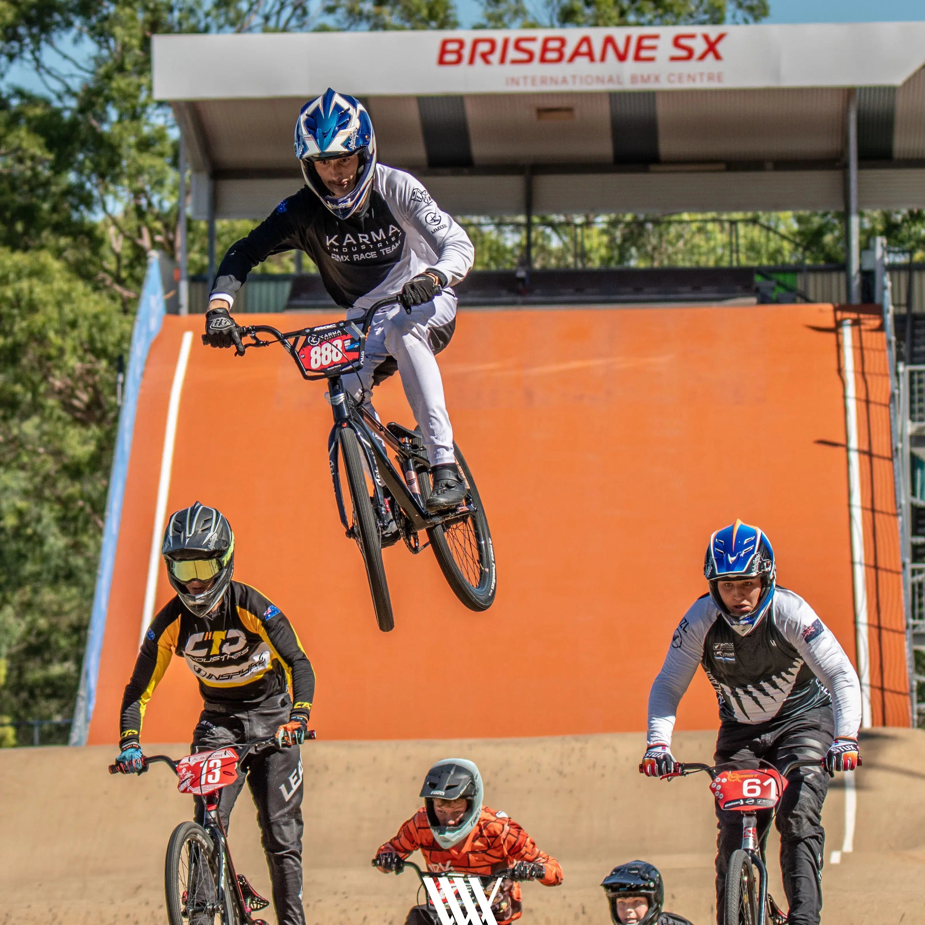 Four BMX riders race on a dirt track—one airborne, three riding below—in action shots from the "LUXBMX Race Photo Packages - Lake Macquarie National Series May 2025." The event sign is visible in the background.