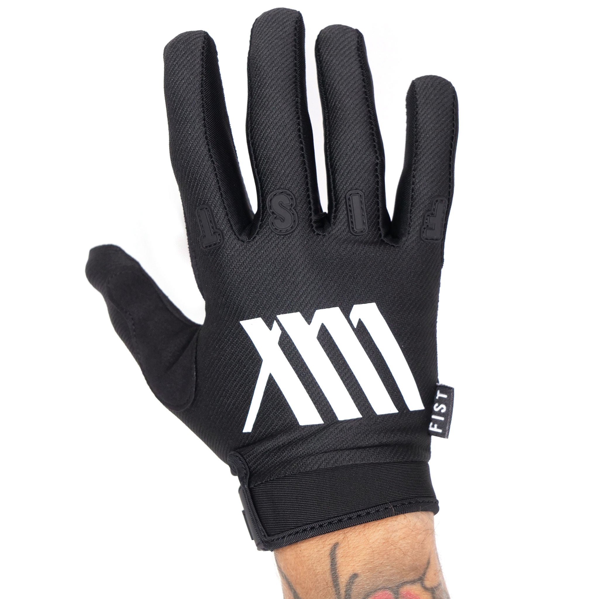 A LUXBMX X FIST V2 glove in black and white, featuring "FIST" across the fingers and "XM" prominently displayed on the back, worn on a tattooed hand. These gloves are ideal for BMX enthusiasts, providing both style and protection, and are available at LUXBMX.