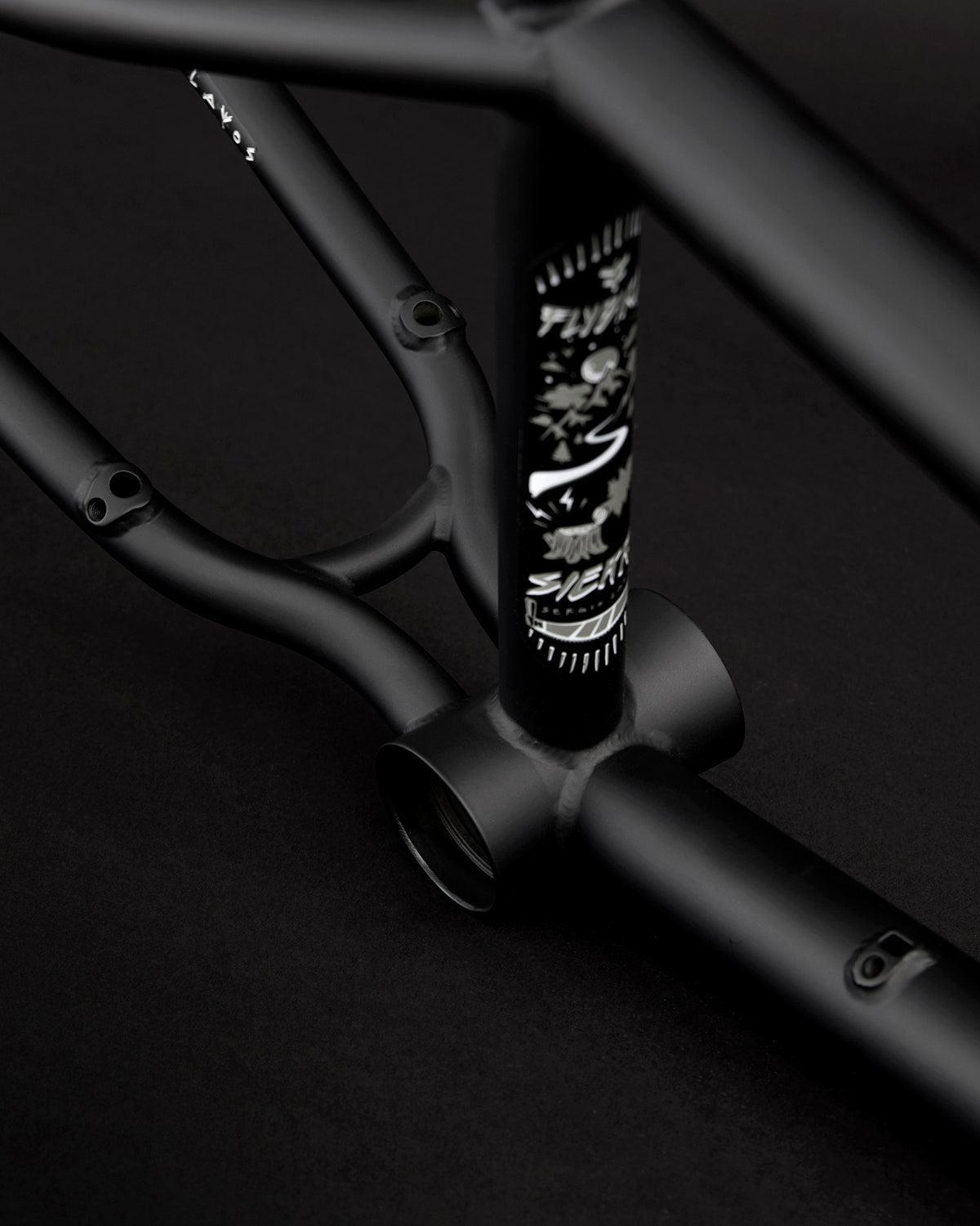Close-up of a matte black Fly Bikes Sierra 18" BMX frame with branding details, showcasing the Sergio Layos signature design against a dark background.