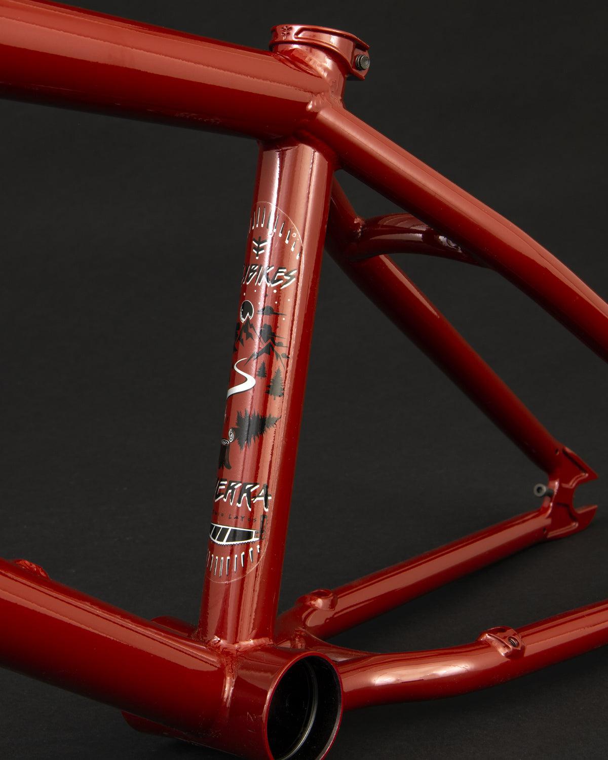 The Fly Bikes Sierra 18 Inch Frame, with its eye-catching black and white decals, contrasts sharply with the dark background, showcasing a sleek design reminiscent of Sergio Layos's bold signature red bicycle frame.