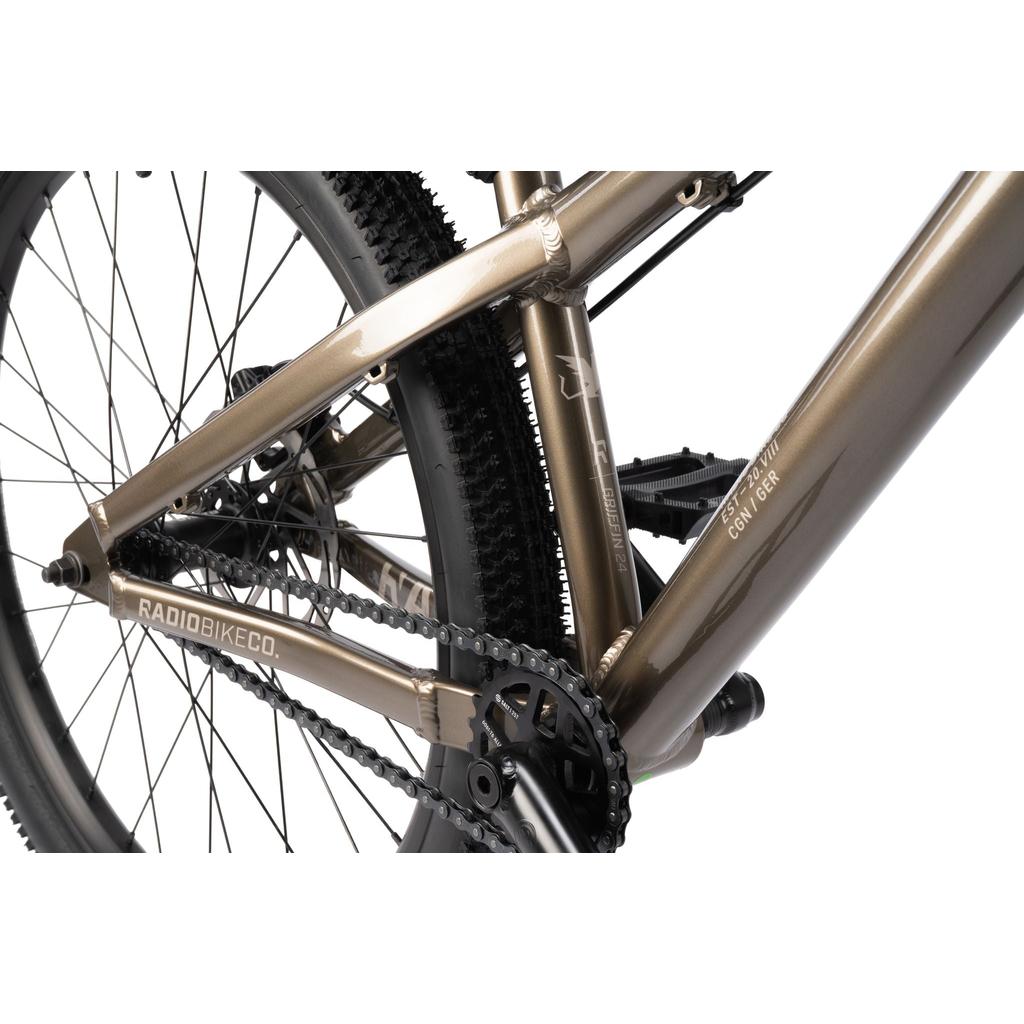 Close-up of the Radio Griffin 24 Inch Dirt Jumper Bike in metallic brown, highlighting the rear wheel, chain, crankset, and frame with "RADIOBIKECO." branding.