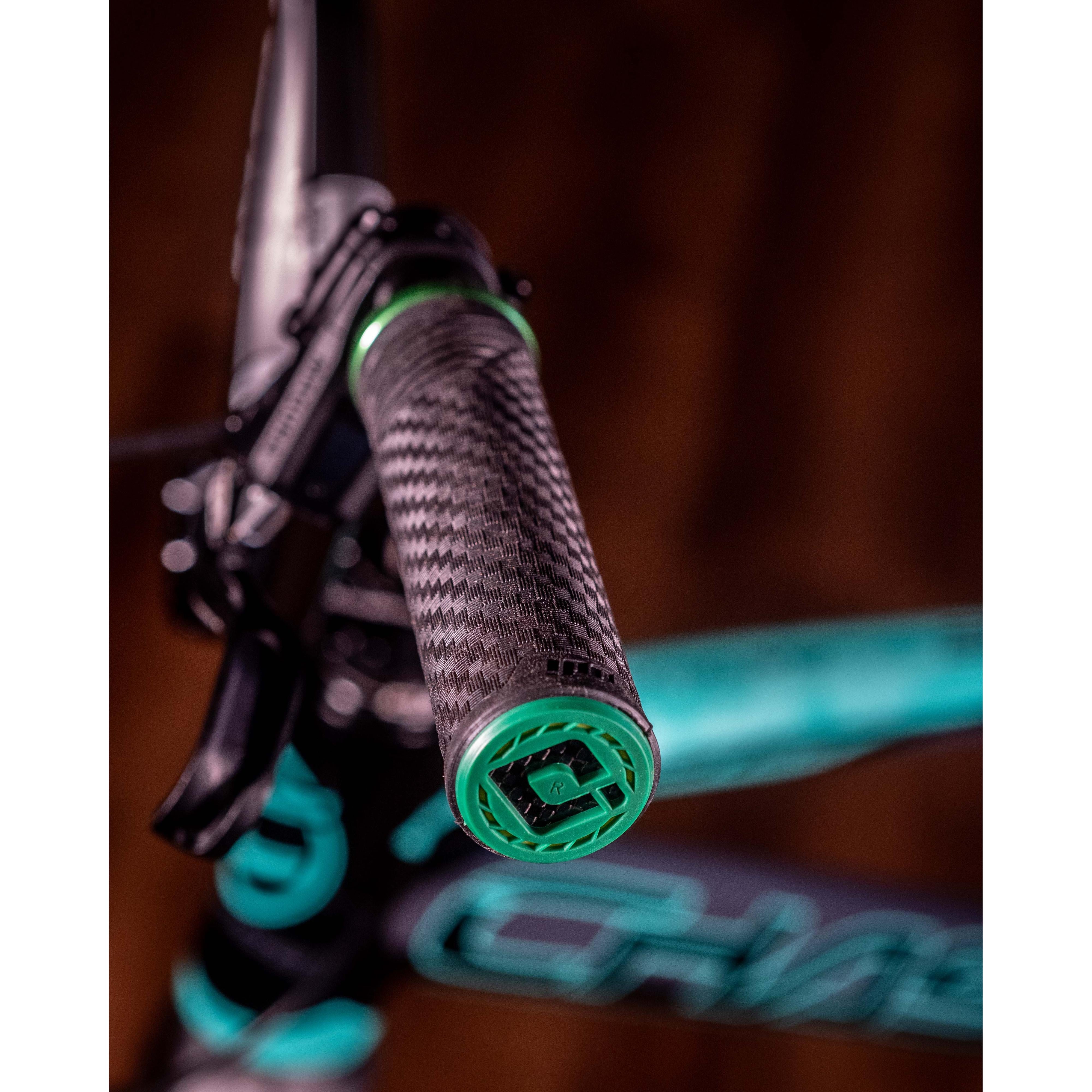 Close-up of the ODI CF Lock On Grips V2.1 Izaac Kennedy Signature, showcasing a carbon fiber pattern and a green end cap, set against a blurred background.