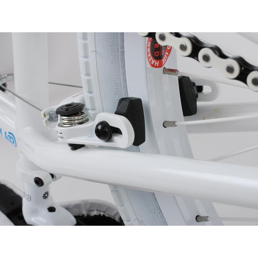 Close-up of a white bicycle's rear brakes and chain, showcasing the brake mechanism featuring Odyssey Ghost Pads and part of the gear system.