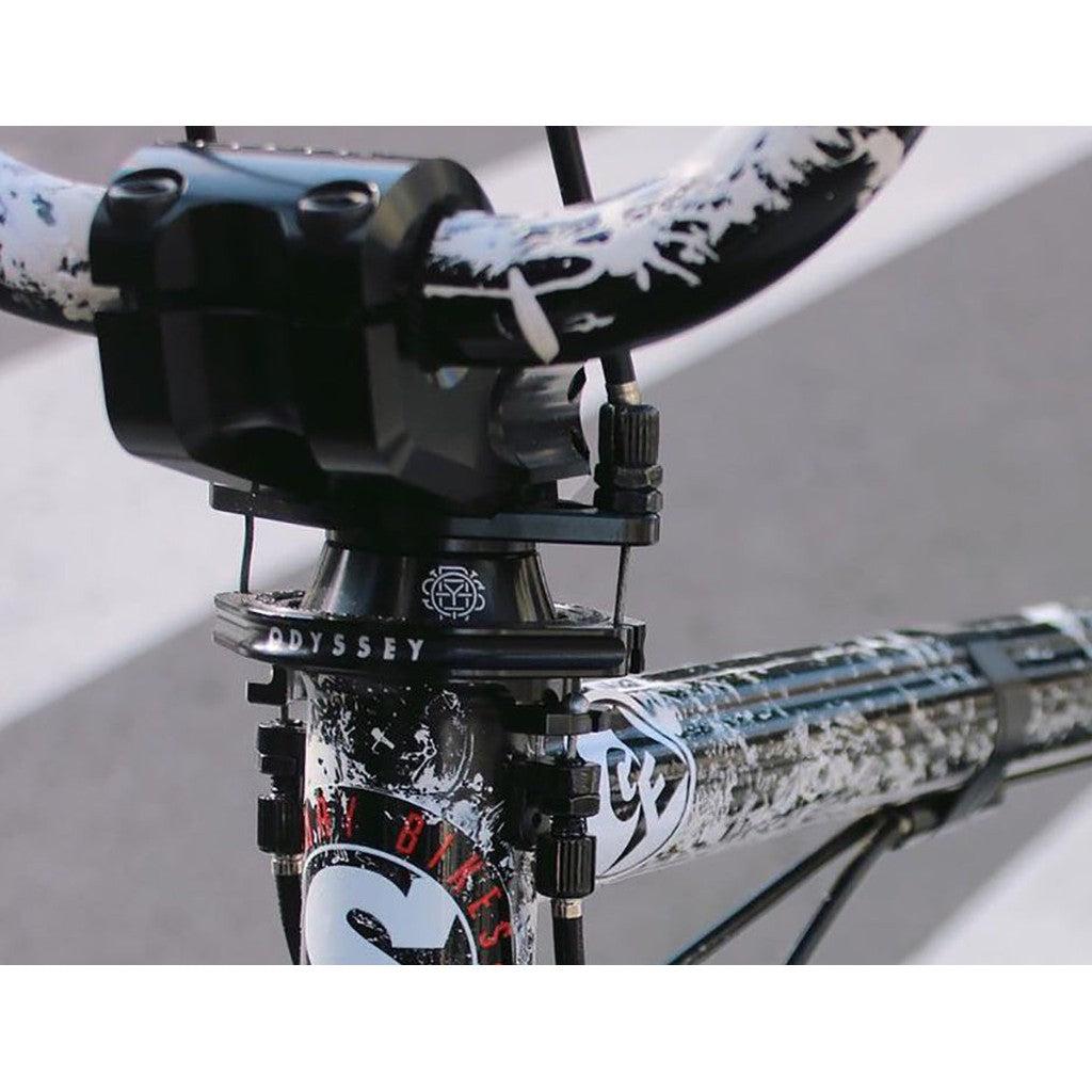 A close-up view of a BMX bike handlebar and stem showcases a black and white color scheme, brand logos, and an Odyssey GTX-S Pro Gyro Kit for seamless bar spins.