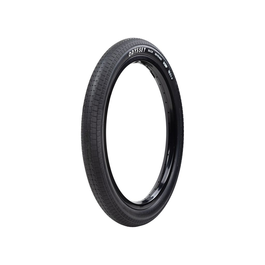 A black, circular Odyssey Super Circuit Foldable Tyre with a textured tread is set against a plain white background. The product name "Odyssey" is prominently displayed on the sidewall, making it an ideal choice for BMX racing enthusiasts seeking reliability and performance.