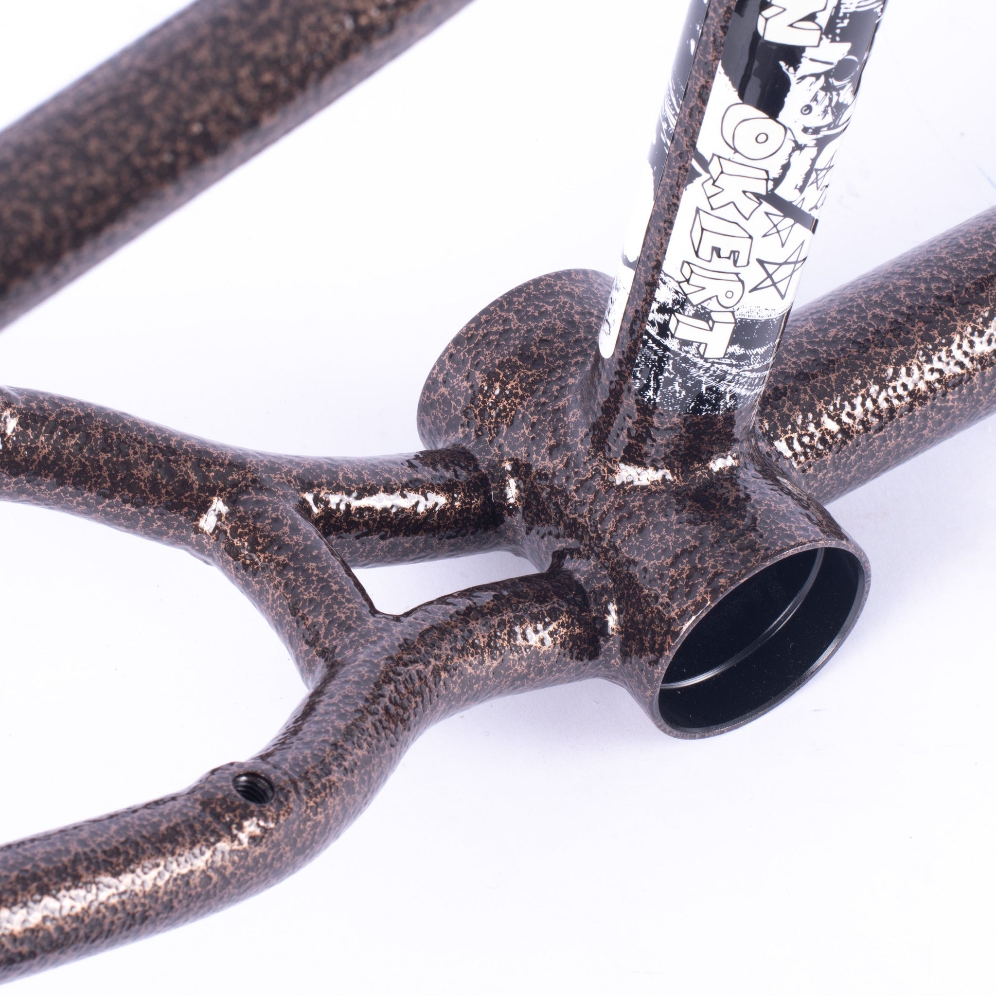 Close-up of a metallic deep bowl bike frame with a speckled brown finish and a partially visible black-and-white graphic sticker on the seat tube, inspired by the Cult Walsh Frame (Preston Okert Signature).