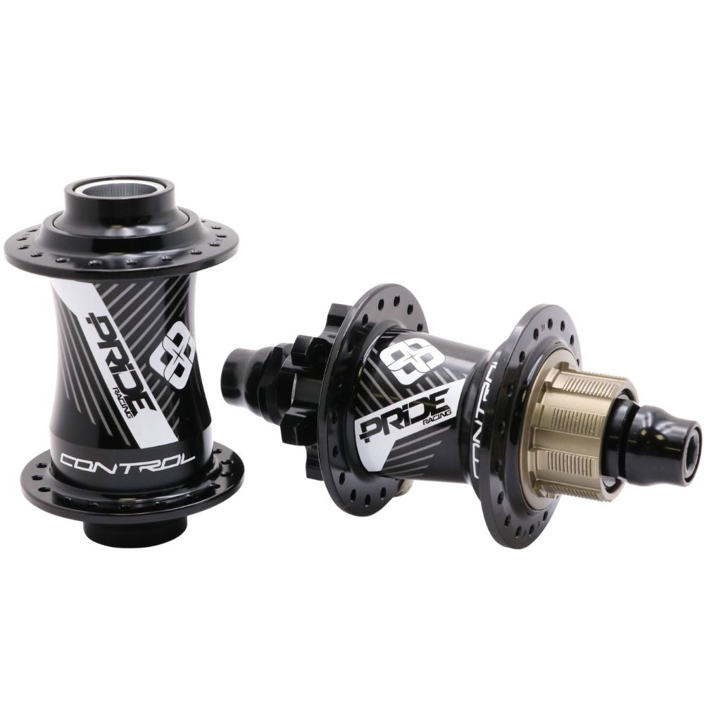 The Pride Control V2 Pro 36H 10mm Hubset features two black CNC machined bicycle hubs with a geometric design and the words "PRIDE" and "CONTROL." One hub is upright, while the other is angled to show off its metallic freehub body. These hubs are perfect for BMX racing and are disc brake ready, making them ideal for performance enthusiasts.