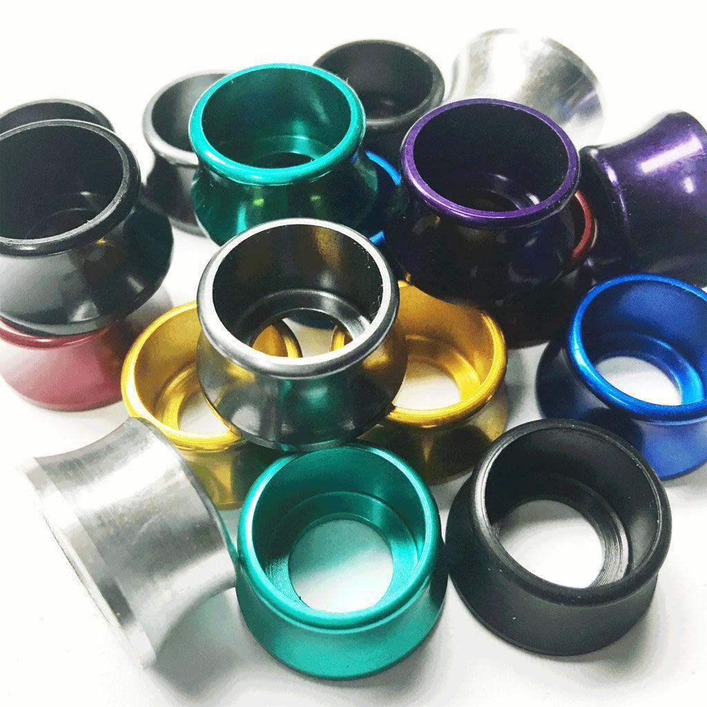 A vibrant mix of aluminum Axle Volcano Washers in green, blue, black, gold, silver, red, and purple—similar to Profile Racing's—scattered on a pristine white surface.