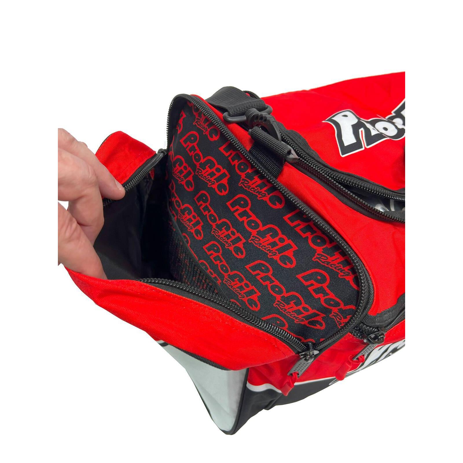A red and black Profile Racing Custom Team Gear Bag, featuring the "Profig" logo, unzips to show its branded interior. Made from durable 600D polyester with a waterproof lining, it keeps essentials safe. A person's hand grips the zipper.