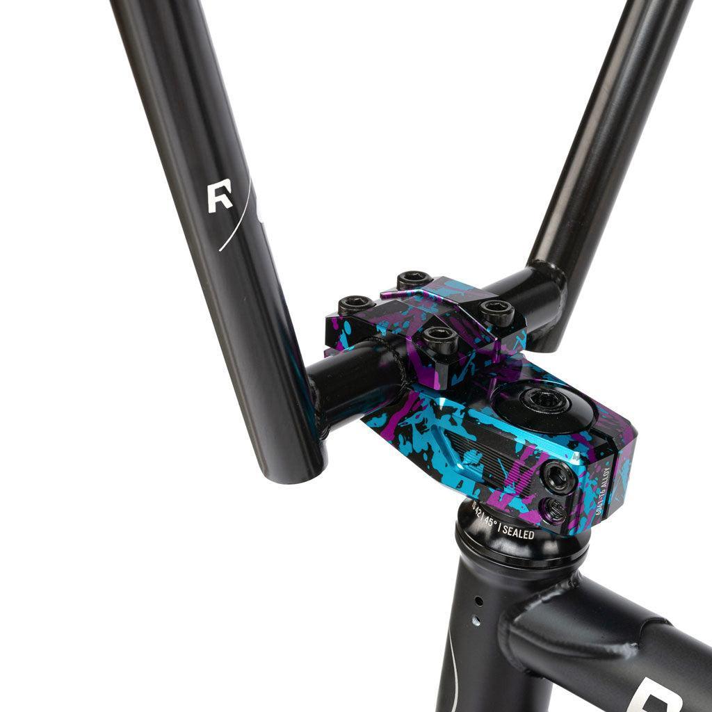 Close-up of a Radio Comrad 20 inch Bike handlebar featuring a colorful, splattered stem design on a black metal frame.