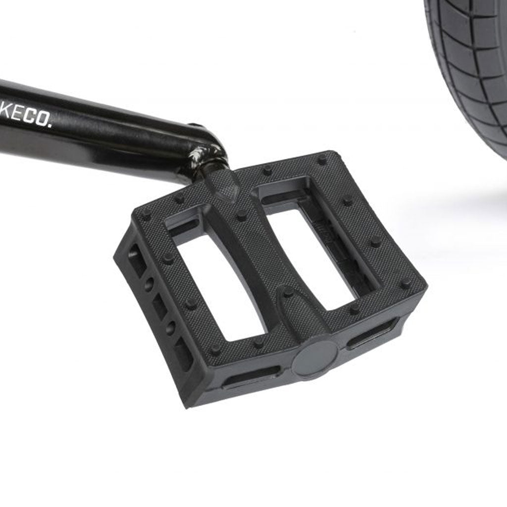 Close-up of a black pedal attached to the crank arm of the Radio Comrad 20 inch Bike, with part of its BMX tire visible.