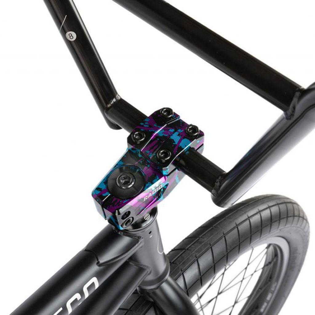 Close-up of the Radio Comrad 20 inch BMX bike handlebar with a colorful stem, black grips, and a black front wheel, highlighting the precision of the Salt Integrated Headset.