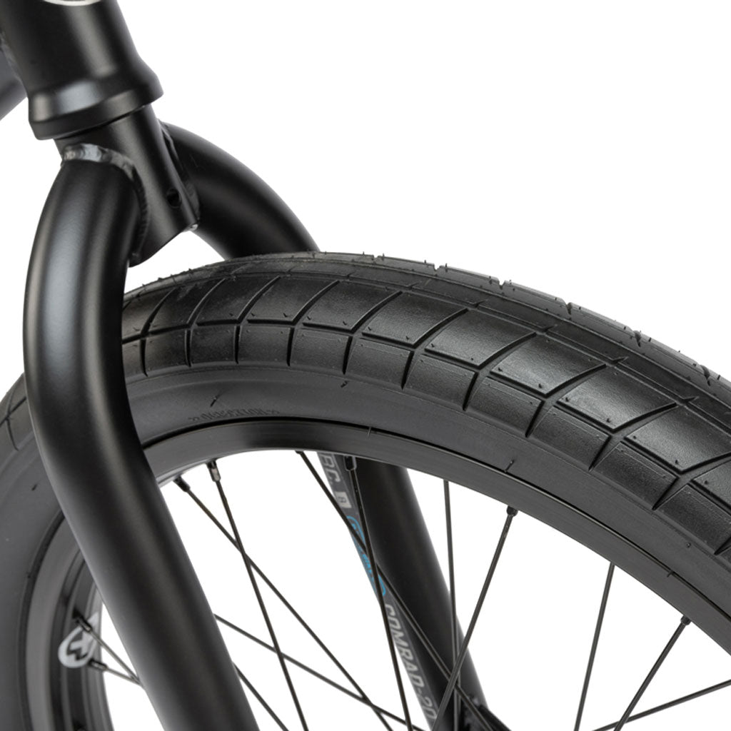 Close-up of the Radio Comrad 20 inch bike's black front wheel with a textured tire, spokes, and fork, featuring the high-quality Salt Integrated Headset.