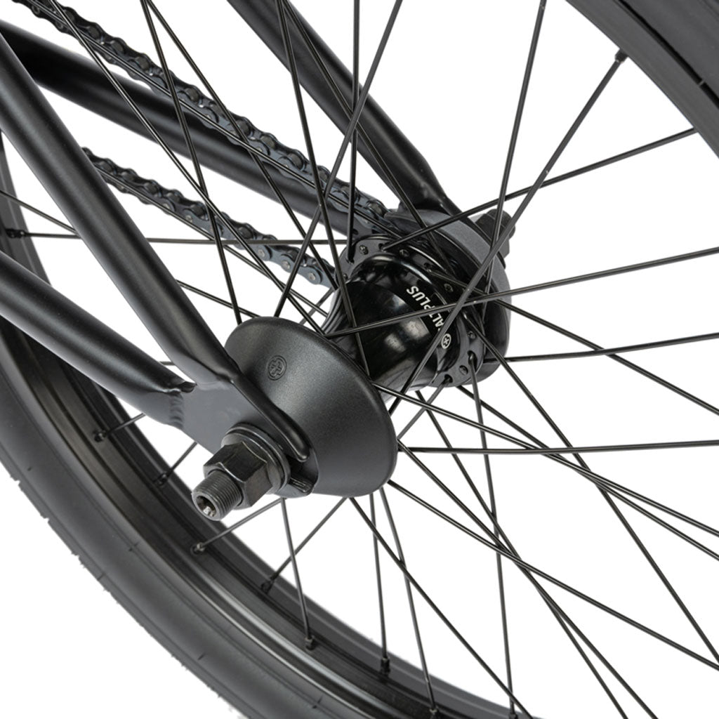 Close-up of a Radio Comrad 20 inch Bike wheel featuring black spokes, rim, and tire, with brand details on the hub and the chain visible in the background.