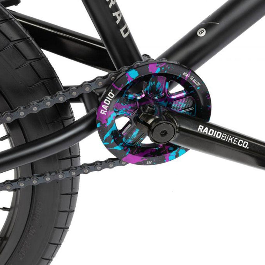 A close-up of the Radio Comrad 20 inch Bike crankset shows a colorful chainring, a full Cromoly frame, and a black chain. The "RADIOBIKECO" branding is prominently featured, complemented by a Salt Integrated Headset for seamless performance.