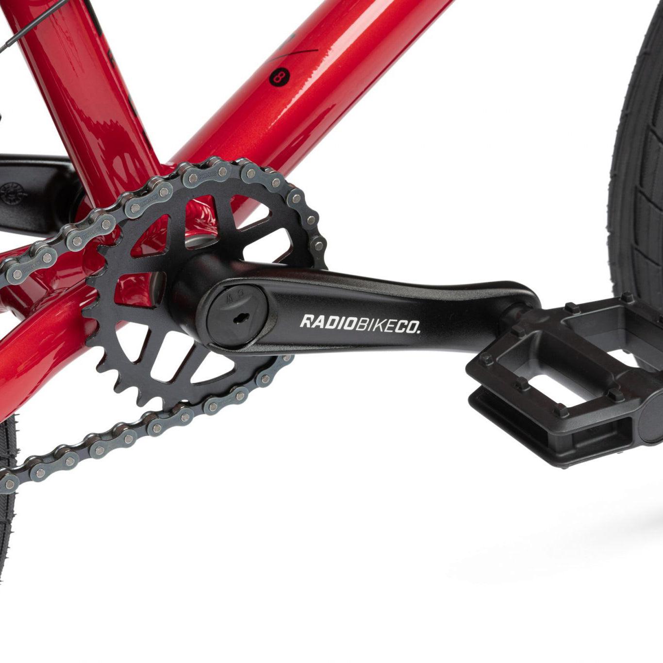 Close-up of a black pedal and crankset with "Radio Bike Co." branding on a red Radio Dice 16 Inch Bike, featuring sturdy 6061 Alloy construction.