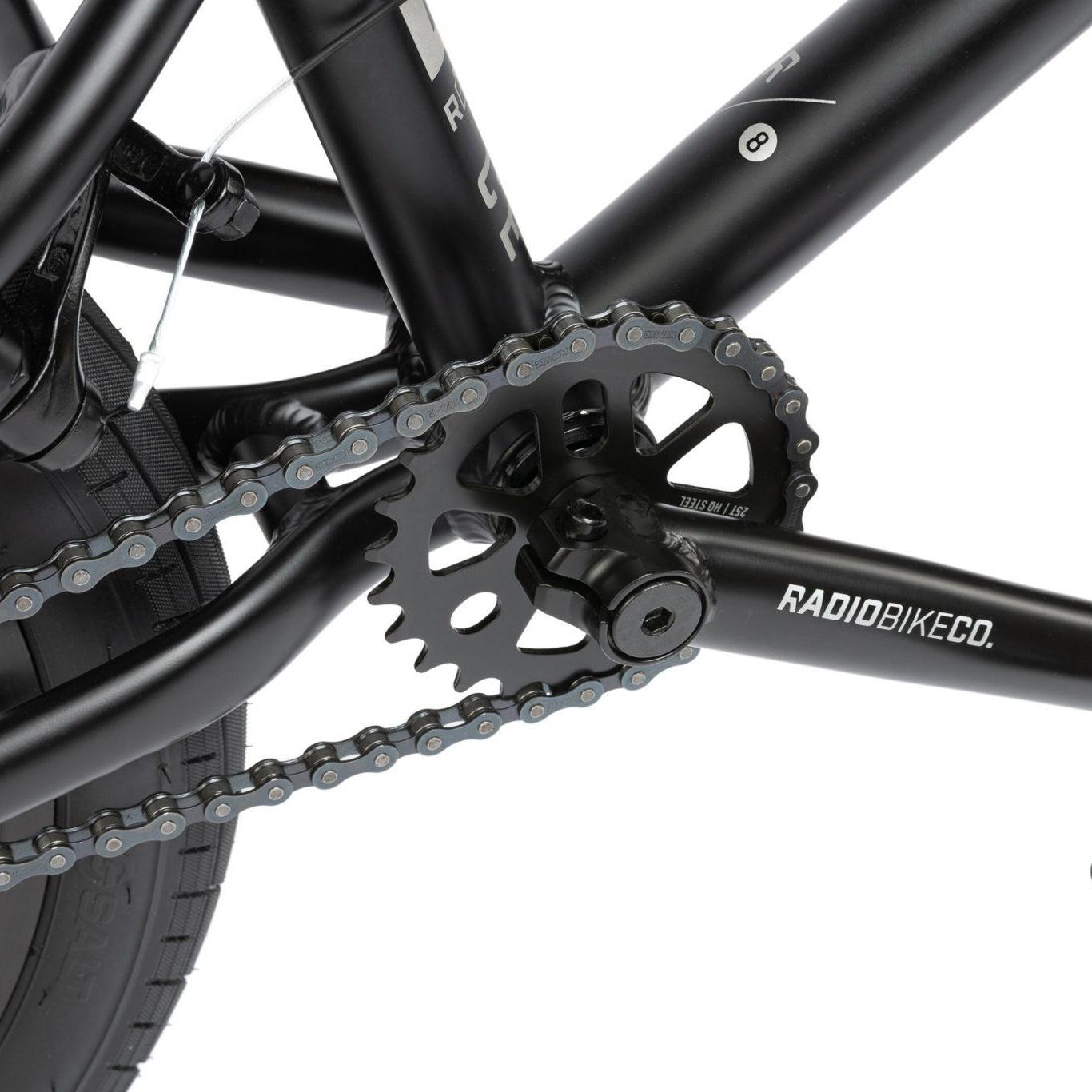 Close-up of a black bicycle's drivetrain, showcasing the chain, sprocket, and Radio Dice 18 Inch Bike with "RADIOBIKECO" branding.