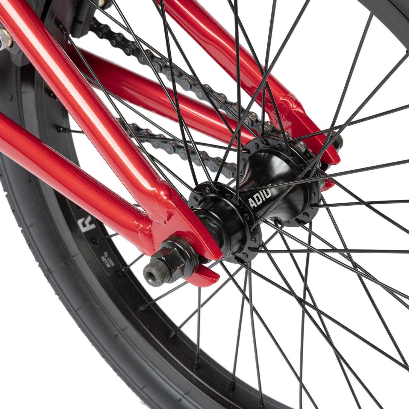 Close-up view of a bicycle's rear wheel hub with black spokes and a red frame. The tire is a black Radio brand with visible tread. The chain, axle nuts, and part of the frame are also visible on this Radio Dice 18 Inch Bike.