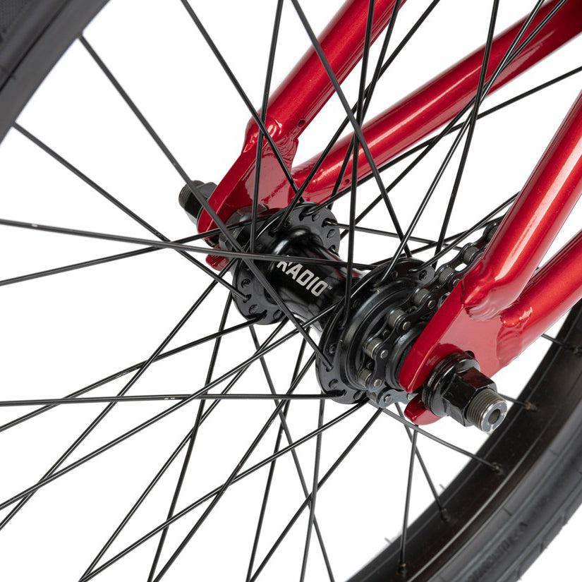 Close-up of a red Radio Dice 20 Inch Bike rear wheel hub with black spokes and a black tire. The brand name "Radio" is visible on the hub.