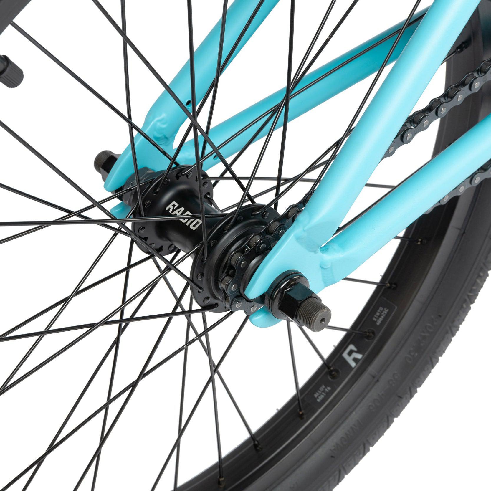 Close-up view of the rear wheel and hub of a turquoise Radio Evol 20 Inch Bike, showcasing the high-quality bike parts including spokes, axle, chain, and part of the frame.